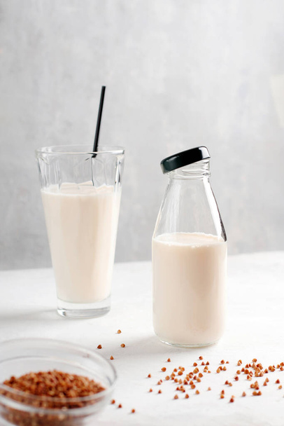 Organic vegan non-dairy buckwheat milk in a bottle and glass on a concrete kitchen table. Gluten and lactose free drink. Vertical position - Fotoğraf, Görsel
