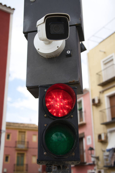 Közelkép a piros közlekedési lámpáról és a térfigyelő kameráról, fókuszálatlan városi háttérrel. Útjelző táblák - Fotó, kép
