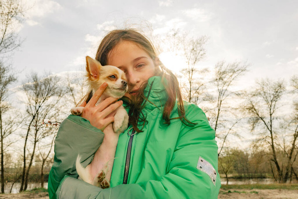 Teenager-Mädchen mit Chihuahua. Mädchen in grüner Jacke mit Welpe auf dem Arm. Chihuahua-Hund mit Mädchen. - Foto, Bild