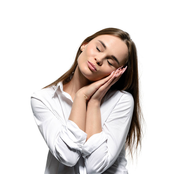 Sweet healthy sleep concept. Young beautiful woman with eyes closed shows a healthy sleep gesture. Isolated on white background - Φωτογραφία, εικόνα