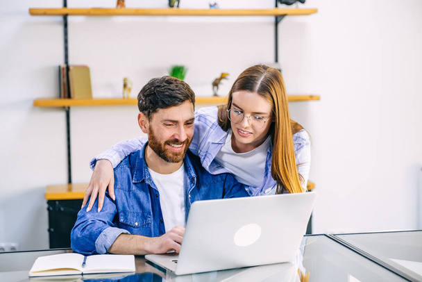 Image of a successful couple of brunettes, man and woman working together on laptop while sitting at the table at home. - Photo, image