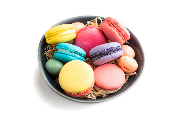 Multicolored macaroons and chocolate eggs in blue ceramic bowl isolated on white background. side view, close up, still life. Breakfast, morning, concept. - Photo, Image