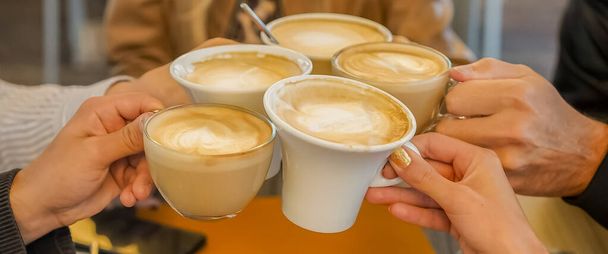 Group of friends drinking coffee  in bar and toasting with each other- Hands with cups of cappuccino in cheers mood - Photo, Image