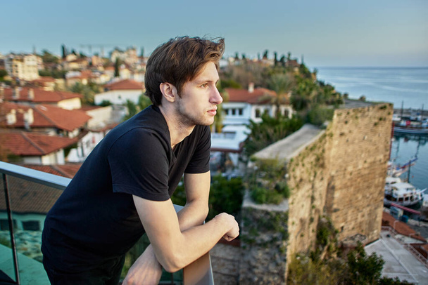 Slender European man, about 20 years old, sadly looks at old city in Antalya from observation point. - Fotó, kép