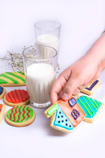 Conceito de viver em casa. Copo de leite e biscoito de mão. Cookies coloridos colocados ao lado dele na mesa no fundo branco. - Foto, Imagem