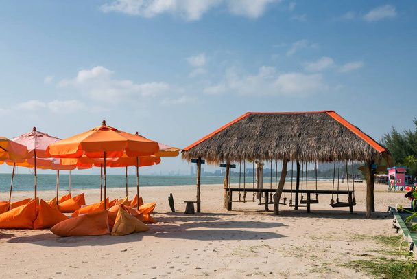 Sedili beanbag arancioni e ombrellone in spiaggia e cabina in legno con sedie a sospensione in riva al mare e cielo blu sulla spiaggia di Cha-am, Petchaburi, Thailandia. Vacanze estive o vacanze in un paese tropicale. - Foto, immagini