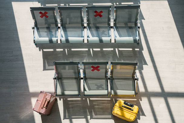 Chaises d'attente avec pancarte de distance sociale et valises ou bagages à l'aérogare pendant la pandémie COVID-19 en vue de dessus. Voyage de transport dans la nouvelle normale - Photo, image