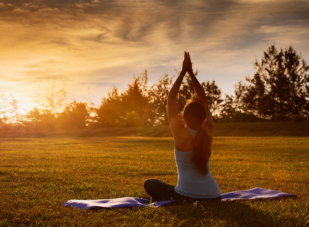Sağlıklı yaşam tarzı ve spor giyimli çekici bir kızın gün batımında dışarıda yoga yaparken lotus pozisyonunda oturmasının rahatlatıcı görüntüsü. - Fotoğraf, Görsel