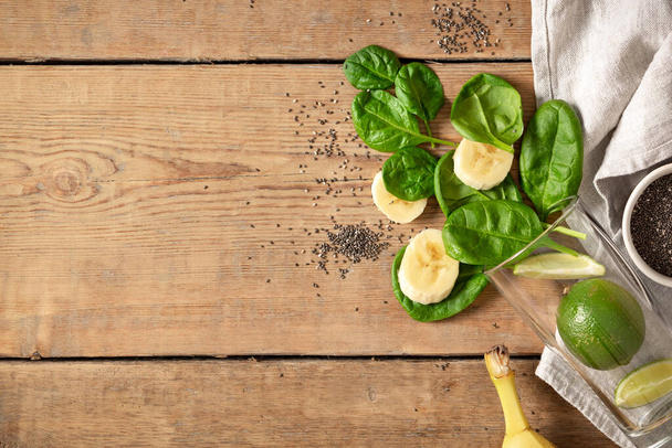 Ingredients for cooking detox smoothie. Rustic style. Glass with spinach, banana, lime and chia seeds on wooden table top view, copy space. Healthy food concept - Φωτογραφία, εικόνα