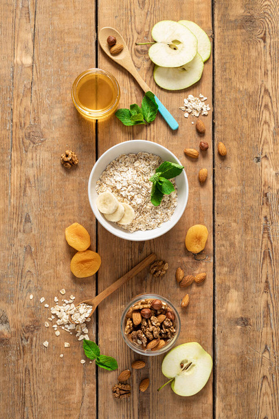 Ingredients for cooking healthy breakfast with oatmeal, dried and fresh fruits, honey and nuts on a wooden table top view. Breakfast table concept - Foto, afbeelding