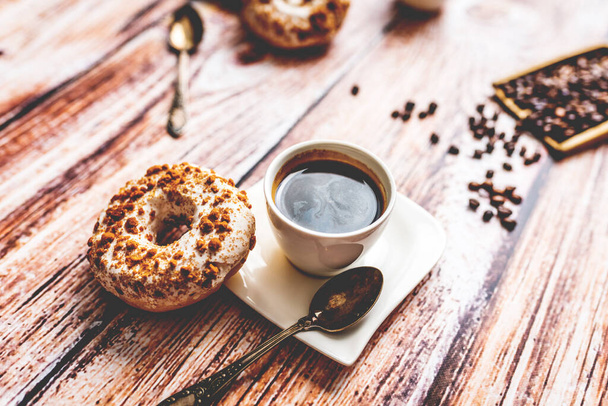Donut branco com polvilhe de chocolate e xícara de café na mesa de madeira  - Foto, Imagem