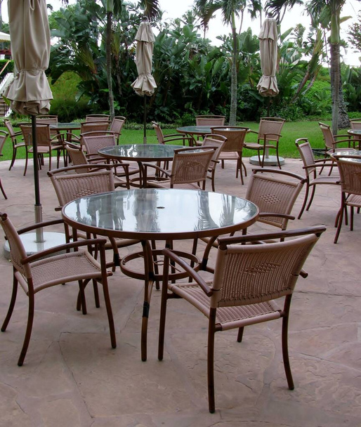 Dışarıda cam masalar, sandalyeler ve katlanmış güneş şemsiyeleri. - Fotoğraf, Görsel