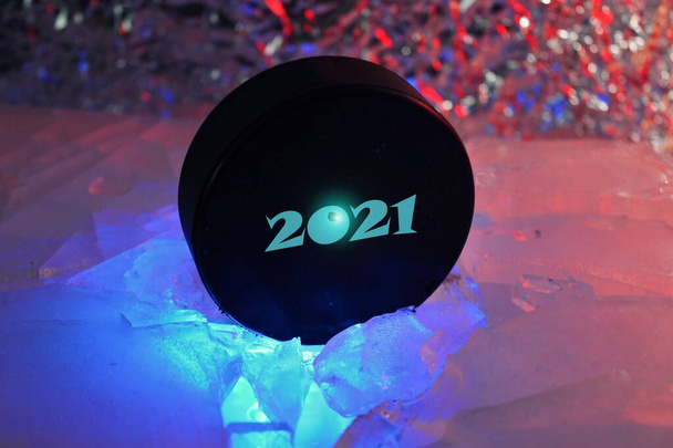 Hockey puck 2021 stands on the edge in cracked ice. A red-blue light falls on him. Czech hockey concept. The hockey puck broke the ice. Long live the World Hockey Championship in 2021. - Photo, Image