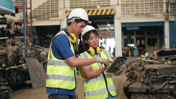 Ázsiai férfi és női munkások egyenruhában és sisakban, Alkalmazottak raktárkészlete az autóalkatrész raktár gyárban. Tabletta segítségével ellenőrizze a régi motorok és a gépi megrendelések autóipari. - Felvétel, videó