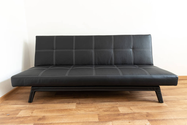 Modern black leather convertible sofa bed, wooden floor. Empty waiting room with a modern black sofa - Φωτογραφία, εικόνα