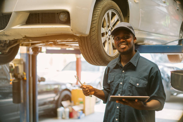 Macho de manutenção Africano verificando o serviço de carro via sistema de seguro na garagem com o uso de tablet - Foto, Imagem