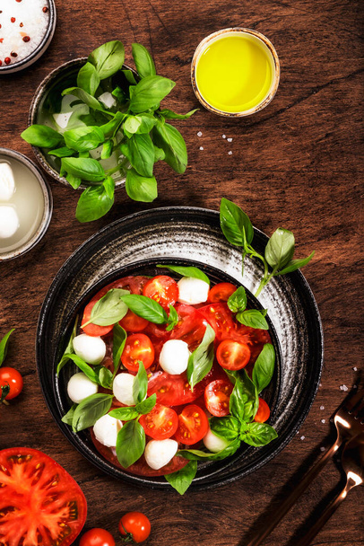 Summer italian salad Caprese with red tomatoes and mozzarella cheese with green basil leaves and olive oil dressing. Top view, wooden table - Fotó, kép