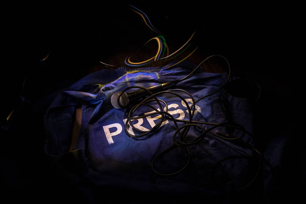 Media Journalism Global Daily News Content Concept. Niebieska kamizelka dziennikarska (prasowa) w ciemności z podświetleniem i mgłą. Mikrofon medialny na kamizelce dziennikarskiej. Skupienie selektywne - Zdjęcie, obraz