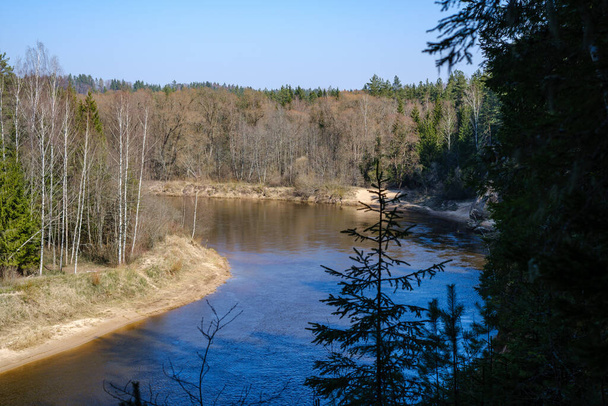 сільська лісова річка з блакитною водою і скелями на березі з весняною рослинністю
 - Фото, зображення