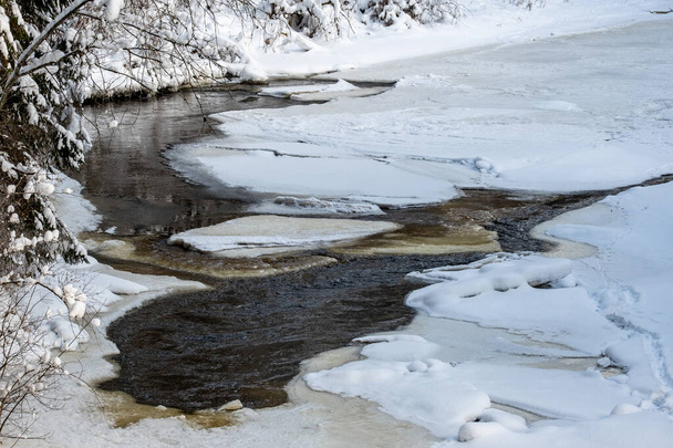 παγωμένο ποτάμι άποψη στο δάσος με πάγο και χιόνι και καφέ νερό κάτω από πάγο. Χειμερινή scebery στην ύπαιθρο - Φωτογραφία, εικόνα
