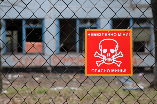 Ozbrojený konflikt východně od Ukrajiny, ukrajinská válka. Červená značka s lebkou a zkříženými hnáty, nápis v ukrajinštině a ruštině - Nebezpečné miny. Pozadí zničené budovy - Fotografie, Obrázek