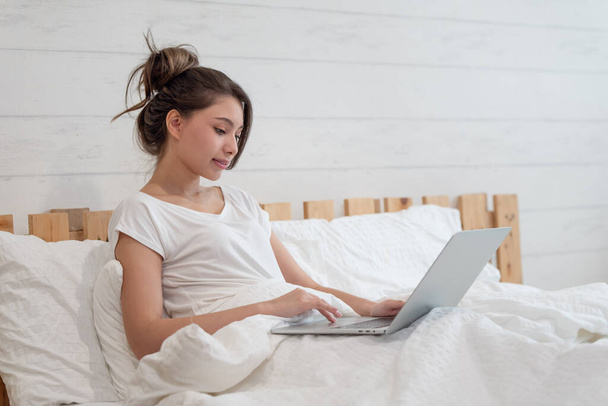 Young woman lying down on bed and using computer in bedroom - Foto, Imagem