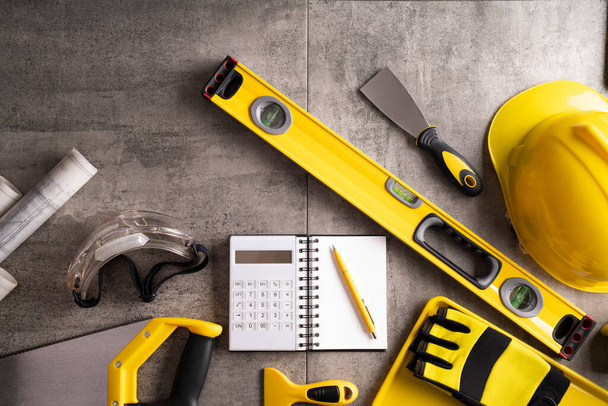Tema del contratista. Kit de herramientas del contratista: hardhat amarillo, libella y herramientas sobre fondo de baldosas grises. - Foto, imagen