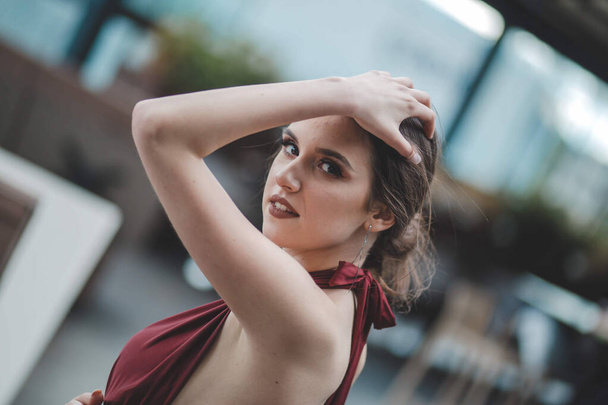 A shallow focus shot of a cute smiling brunette woman in a fancy red dress posing in an outdoor cafe - Fotografie, Obrázek