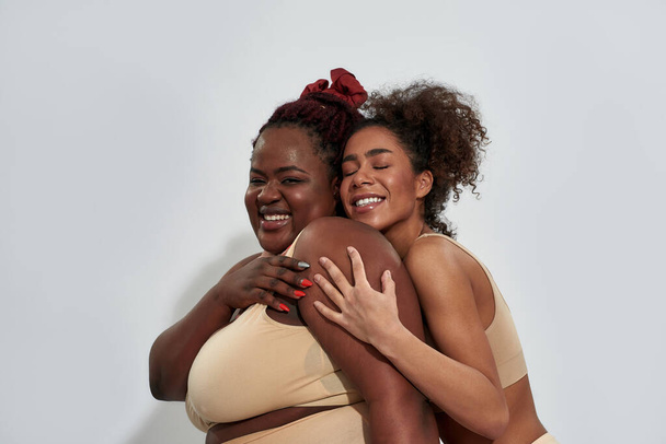 Two happy african american women in underwear with different body size having fun, posing together isolated over gray background - Fotó, kép