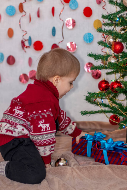 Un bambino all'albero di Natale con ghirlande ci mette dei regali sotto. Emozioni dei bambini. Natale e Anno nuovo. Il concetto di banner pubblicitario. - Foto, immagini