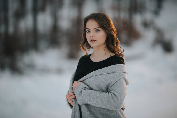 A shallow focus shot of a cute brunette woman posing outside wearing a gray winter coat during sunset - Zdjęcie, obraz