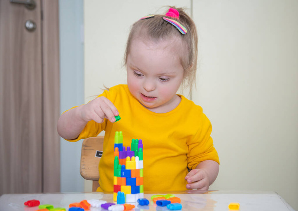 Kaunis tyttö, jolla on Downin oireyhtymä, leikkii rakentajan kanssa, kirkkaat läpinäkyvät luvut, vammaisen lapsen varhainen kehitys. - Valokuva, kuva