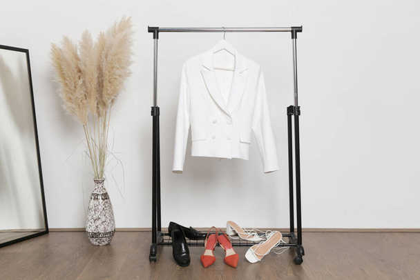 Women's Clothes. Clothes rack, white blazer and shoes in fashion atelier. - Photo, Image