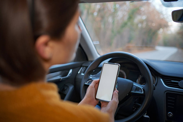 Mockup-Bild einer Frau, die ein Mobiltelefon mit leerem Bildschirm hält und benutzt, während sie ein Auto fährt. Menschen, Fahr-, Navigations- und Transportkonzepte - Foto, Bild