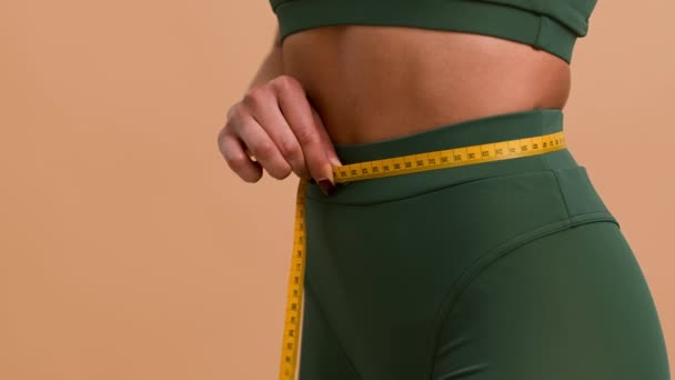 Mujer negra que mide la cintura delgada con cinta, fondo beige, primer plano - Imágenes, Vídeo