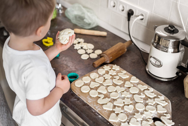 Küçük sevimli çocuk beyaz çocuk evde mutfakta genç yetişkin bir anneyle tatlı kurabiyeler pişiriyor. Anne küçük oğlu ev yapımı tatlı pişiriyor. Ebeveyn çocuk aktivitesi - Fotoğraf, Görsel