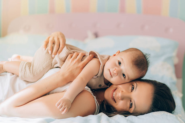 Jonge moeder knuffelt haar gemengde ras kind. Kind adoptie en In Vitro Fertilization IVF. aziatische baby en indisch Moeder liggend op de bed. - Foto, afbeelding