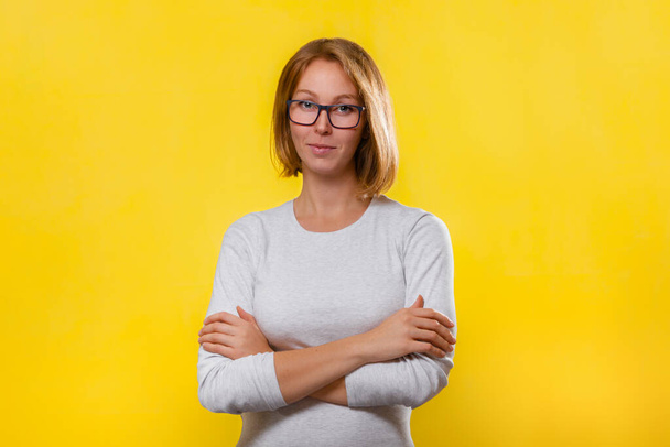 Young blonde woman in glasses posing with her arms crossed. Yellow background. Copy space. - Fotó, kép