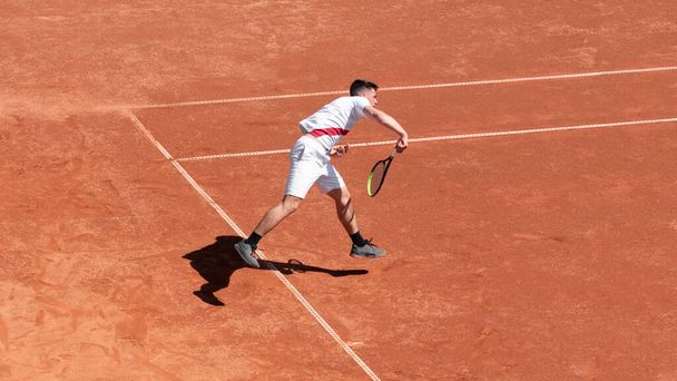 Тенісний гравець в дії на глиняному тенісному корті під час гри. Хоробрість професійного спортсмена в змаганнях. Індивідуальний вид спорту
 - Фото, зображення