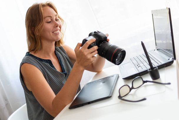 Uma jovem fotógrafa sentada em sua mesa e trabalhando com uma câmera. Fechar. - Foto, Imagem