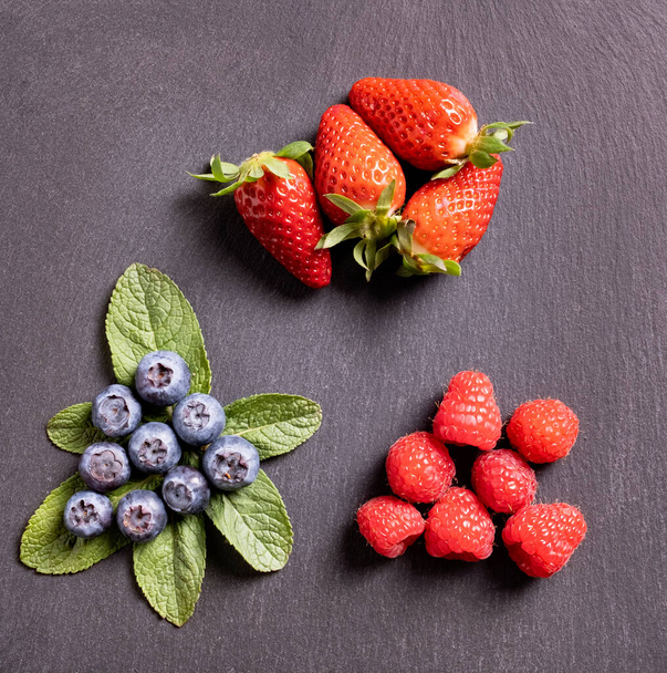 Fresas, frambuesas y arándanos con fondo gris. Alimentos ecológicos - Foto, Imagen