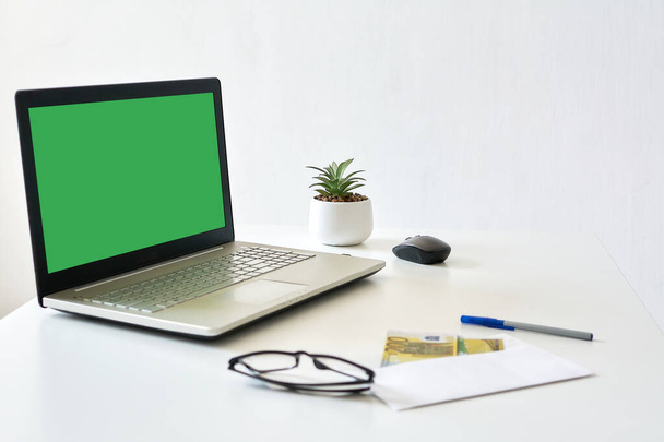 laptop with a blank green screen on a white wooden table against a white wall, mock up - Foto, afbeelding