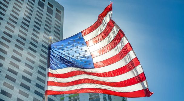 Bandiera americana sventolante retroilluminata con moderni grattacieli della città sullo sfondo. - Foto, immagini
