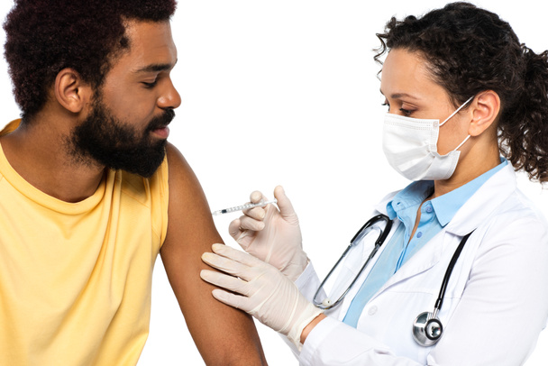 Αφροαμερικανός γιατρός με ιατρική μάσκα κάνει εμβολιασμό των ασθενών που απομονώνονται στα λευκά  - Φωτογραφία, εικόνα
