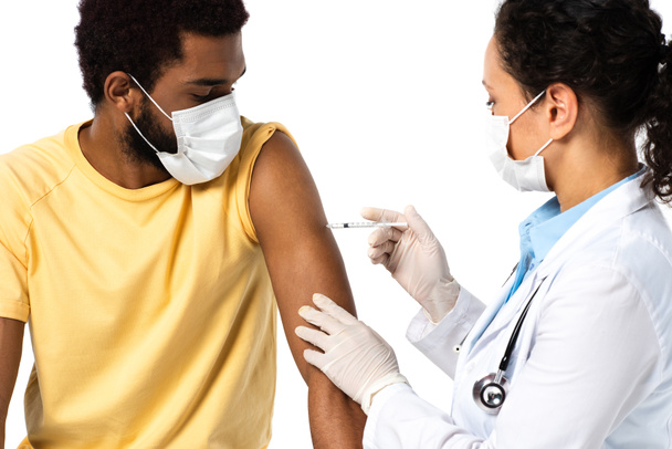 Afrikanisch-amerikanischer Arzt in Schutzmaske und Latexhandschuhen bei der Impfung von Patienten isoliert auf weiß  - Foto, Bild