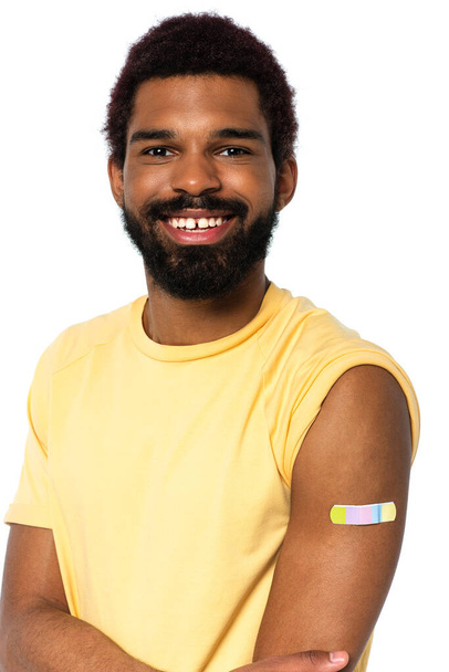 Alegre hombre afroamericano con yeso adhesivo en brazo aislado en blanco  - Foto, Imagen