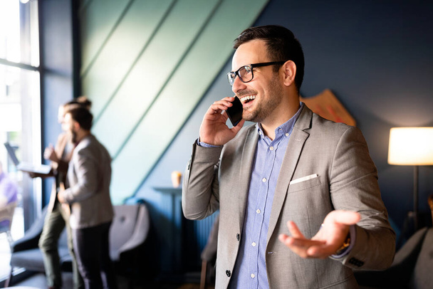 Business, people and office concept. Happy young businessman talking on smartphone in office - Foto, imagen