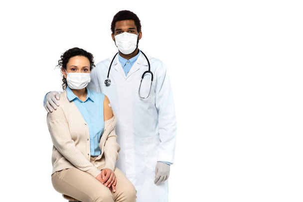 Patient with adhesive patch on arm looking at camera near african american doctor in medical mask isolated on white  - Zdjęcie, obraz