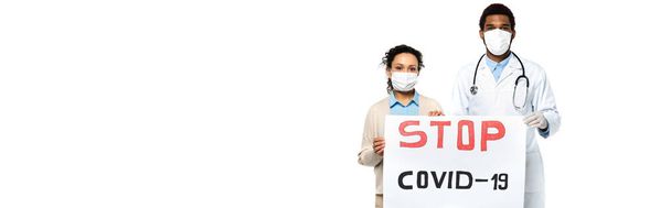 Afrikanisch-amerikanischer Patient und Arzt in medizinischen Masken mit Plakat mit Stop Covid-Schriftzug auf weißem Hintergrund, Banner  - Foto, Bild