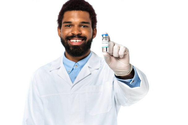 Βάζο με το εμβόλιο στο χέρι του Αφροαμερικανού γιατρού χαμογελώντας σε θολή φόντο απομονωμένο σε λευκό  - Φωτογραφία, εικόνα